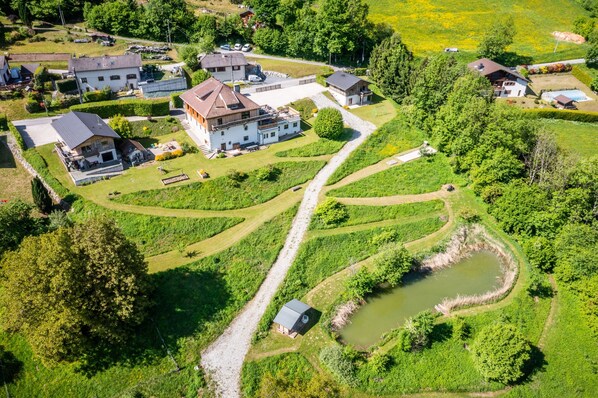 An aerial view of a residential area with multiple houses, a central building with a sloped roof, and a small pond.