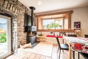 A stone wall, a fireplace, a wooden bench, a table with chairs, and a window with a view.