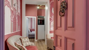 A pink-themed room with a bed, a chair, a door with a lion head knocker, and a kitchen area with a refrigerator and oven. - Apartment 'Royal Suite' with Wi-Fi and Air Conditioning (Firenze)