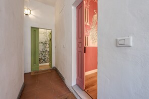 A hallway with a green door, a red door with a peacock design, and a light switch on the wall.