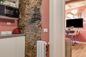 Une cuisine avec un mur en pierre, un four à micro-ondes de la marque Bosch, une bouilloire rouge et une autre bouilloire de la marque THES posée sur le plan de travail.