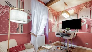 A room with a dining area, a sofa with a red pillow, a table with a book and a glass of wine, and a TV mounted on the wall. - Apartment 'Royal Suite' with Wi-Fi and Air Conditioning (Firenze)