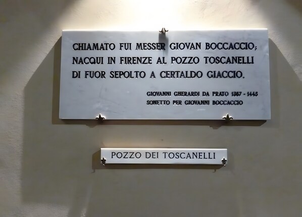 Une plaque blanche avec du texte noir, fixée sur un mur à l’aide d’un support métallique. En dessous, une petite plaque indique : « POZZO DEI TOSCANELLI ».