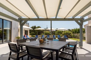 Eine überdachte Terrasse mit Pool, Liegestühlen und einem Tisch mit Stühlen.