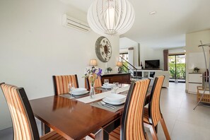 A dining area with a wooden table set for four, striped chairs, a decorative wall piece, and a modern pendant light. - Holiday Home 'Peva' with Private Pool, Wi-Fi and Air Conditioning (Albufeira)
