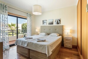 Ein Schlafzimmer mit einem großen Bett, einem Nachttisch, einer Kommode und Blick ins Freie.