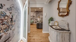 Un couloir avec un papier peint à motifs floraux, un plancher en bois, un miroir et un lit à l’arrière-plan.