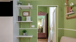 A room with green walls, white shelves, a mirror, a bed, and a door leading to another room.