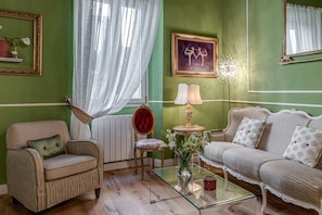 Une pièce avec un mur vert, un fauteuil à rayures, une chaise rembourrée de couleur rouge, un canapé blanc, une table basse en verre et un tableau encadré accroché au mur.