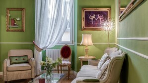 A room with a green wall, a glass coffee table, a red chair, a white sofa, and a lamp.