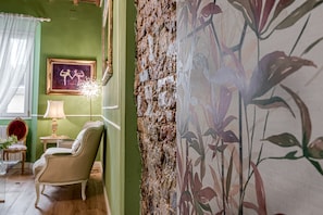 Une pièce avec un mur vert, un papier peint à motifs floraux, un tableau encadré, une lampe, une chaise et un mur à texture.