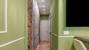 A narrow hallway with green walls, a wooden floor, a door at the end, and a white switchboard on the right.