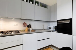 Una cucina moderna con mobili bianchi, piano cottura a gas, microonde e forno nero.