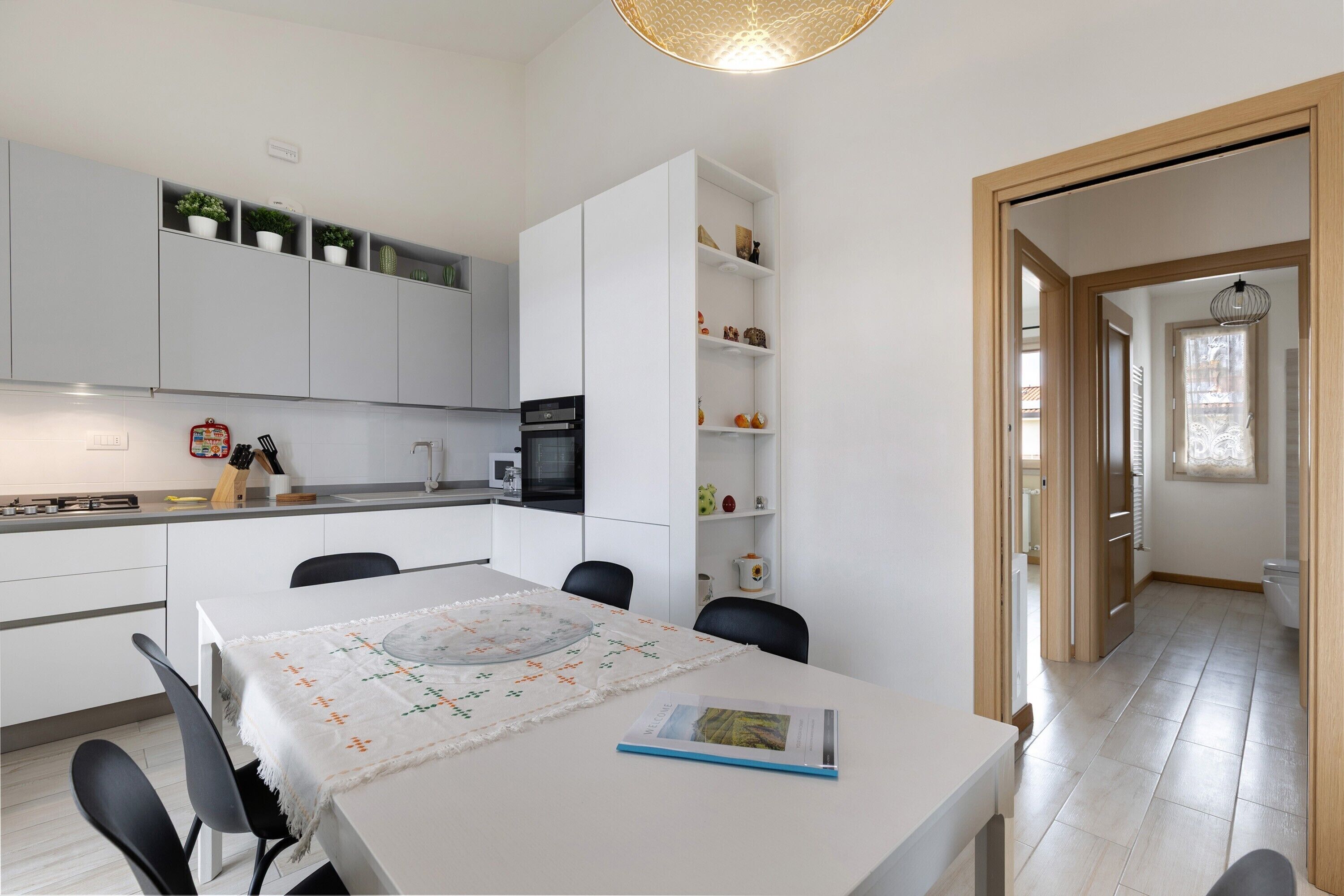 Une cuisine moderne avec des meubles blancs, une table à manger avec des chaises et un petit îlot central doté d’un évier.
