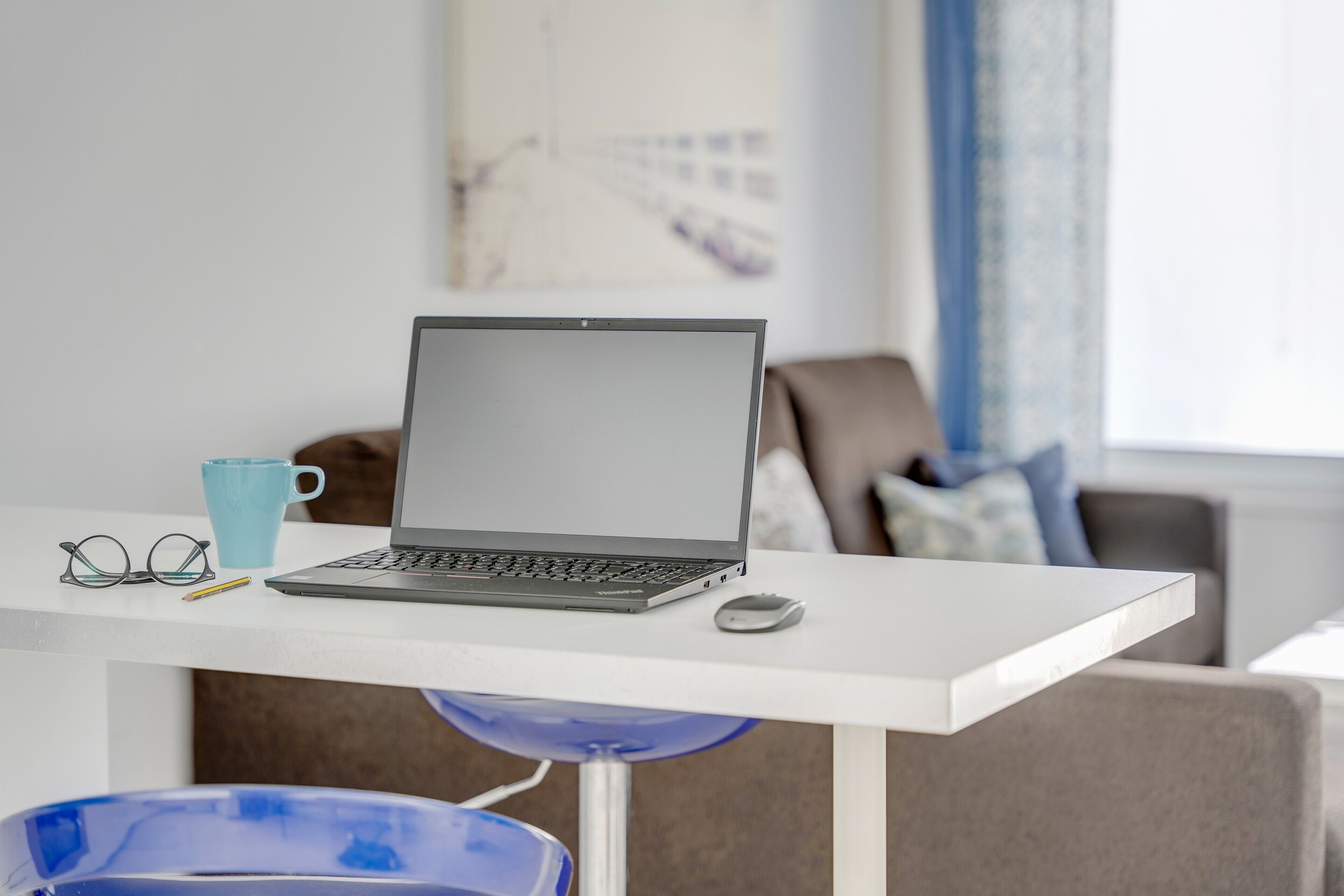 Ein Laptop auf einem weißen Schreibtisch mit blauem Stuhl, Brille und Tasse.