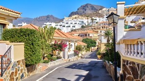 A narrow street lined with white buildings, stone walls, and greenery.