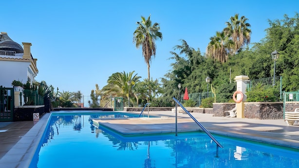 A swimming pool with a clear blue water surface, surrounded by palm trees and a building with a dome-shaped roof.