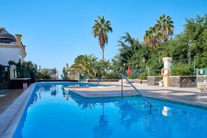 A swimming pool with a clear blue water surface, surrounded by palm trees and a building with a dome-shaped roof. - Vacation 'Pearl Of Windsor Park' with Sea View, Wi-Fi and Air Conditioning (Costa Adeje Tenerife)