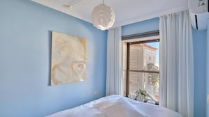 A bedroom with a bed, a ceiling light, a window with curtains, and a wall-mounted painting.