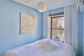 A bedroom with a bed, a ceiling light, a window with curtains, and a wall-mounted painting.