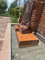 Una escultura de una figura sobre un pedestal con un diseño circular, ubicada en una pared de ladrillo.