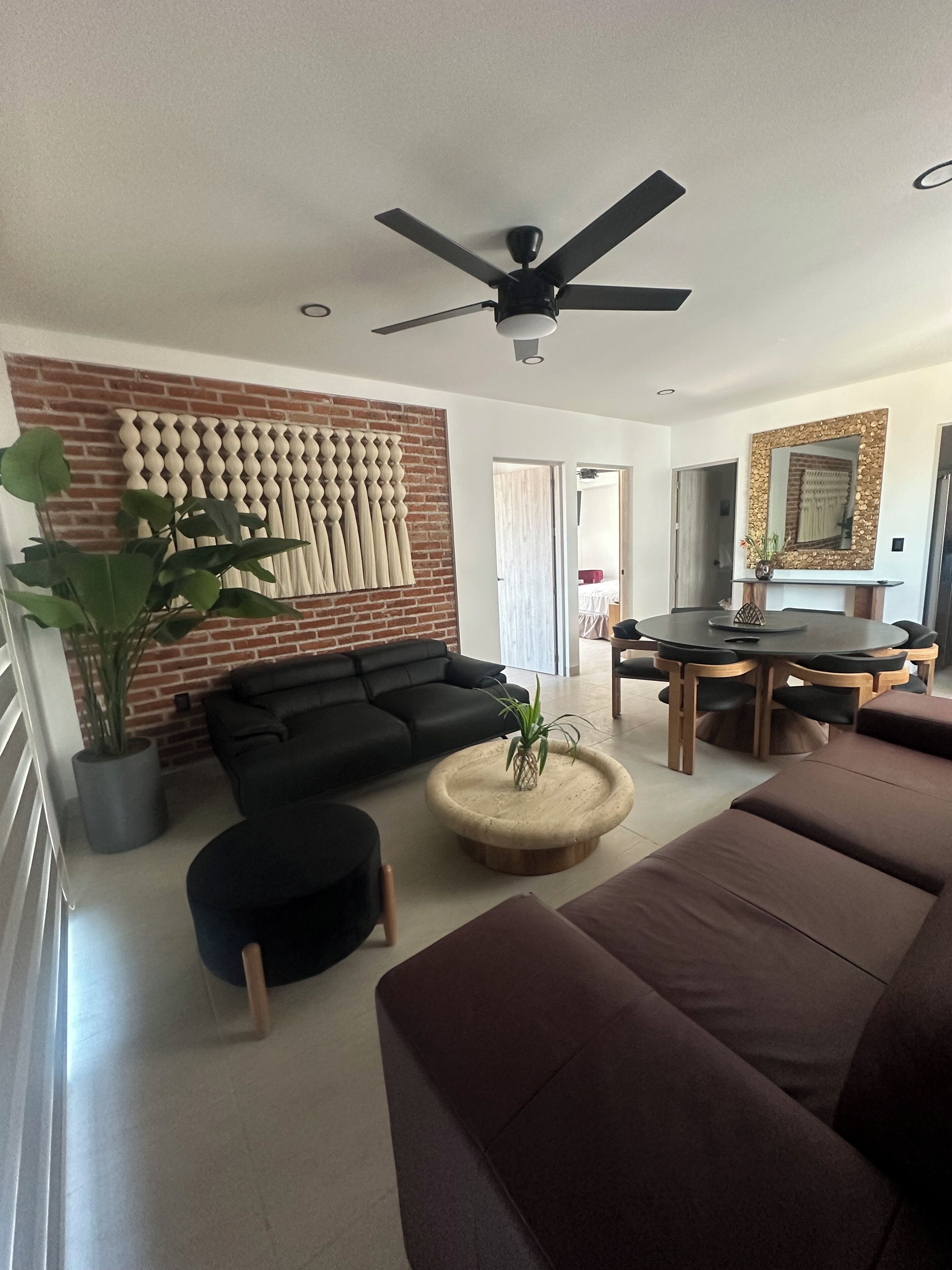 A modern living room with a black sofa, a round coffee table, and a dining area with a wooden table and chairs.