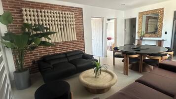 A modern living room with a black sofa, a round coffee table, and a dining area with a wooden table and chairs.