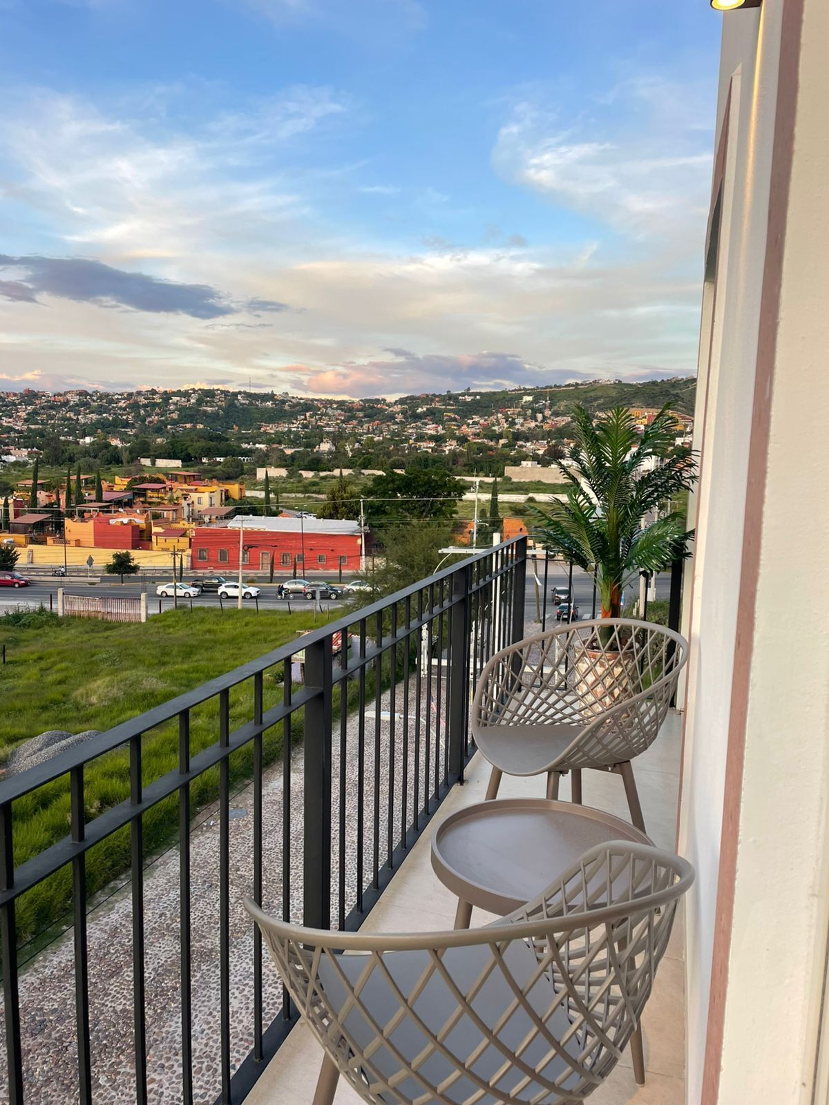 Un balcón con dos sillas y una maceta, con vista a una zona residencial con casas y una calle.