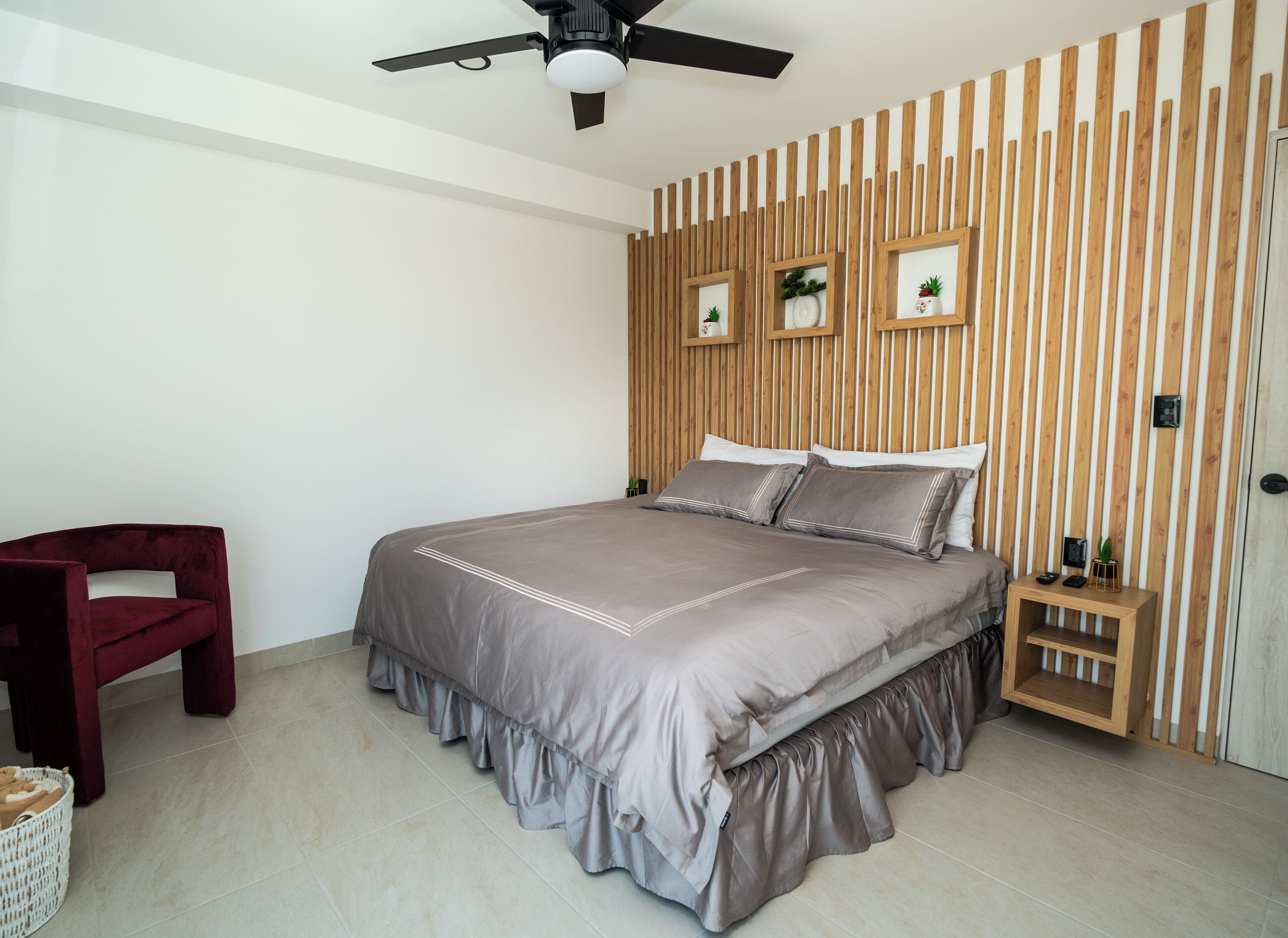 A bedroom with a bed, a chair, a bedside table, and a wooden slatted wall.