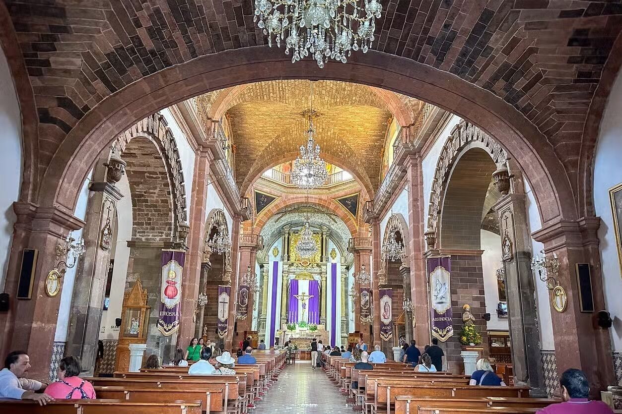 An interior of a church with arched ceilings, pews, and a central altar.