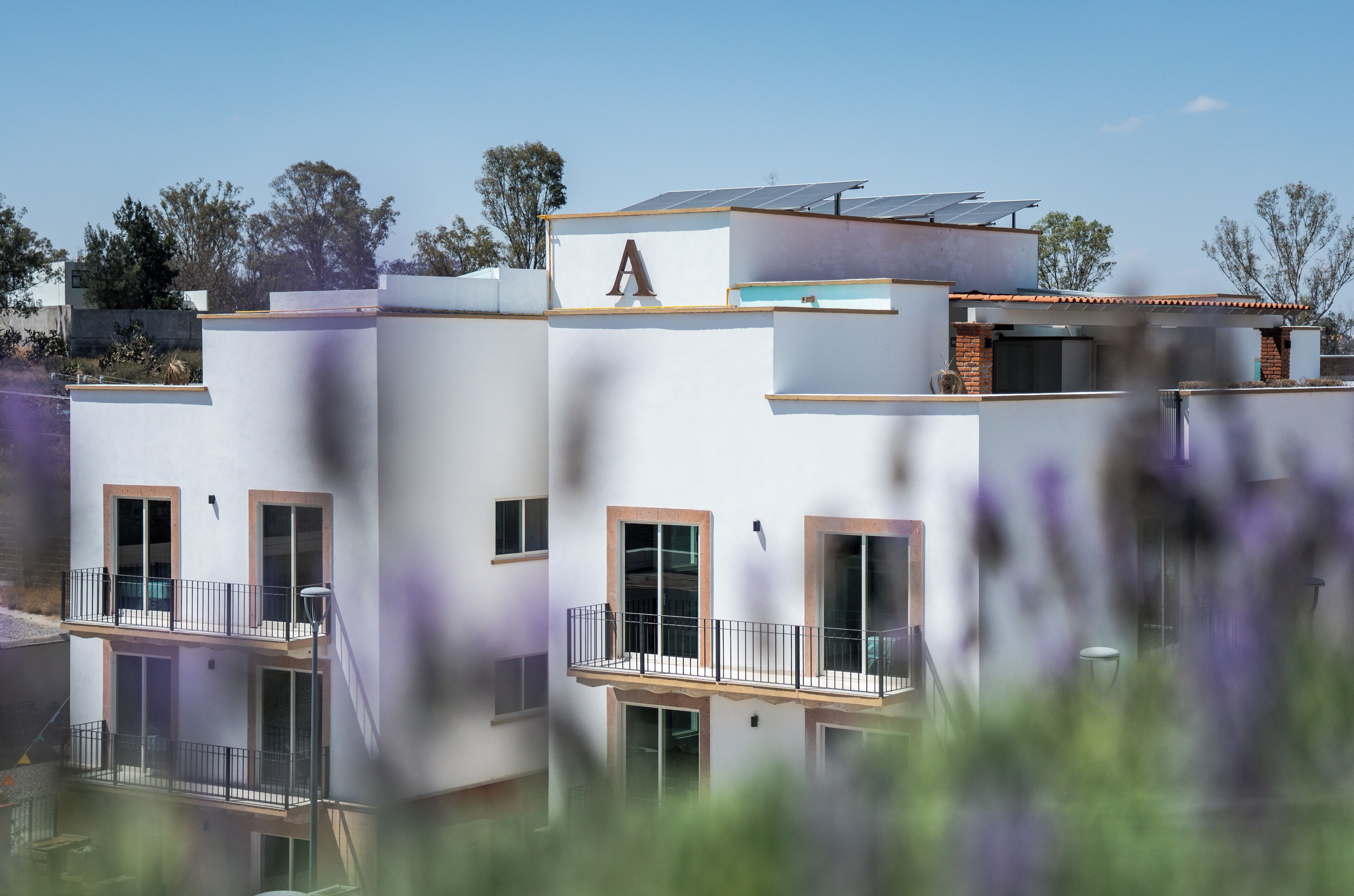 Un edificio moderno con una 'A' destacada en la fachada, balcones y paneles solares.