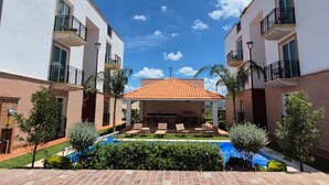Un patio con piscina, sillas de descanso y una zona de estar cubierta.