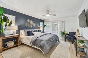 A bedroom with a bed, a nightstand, a chair, a TV, and a ceiling fan.