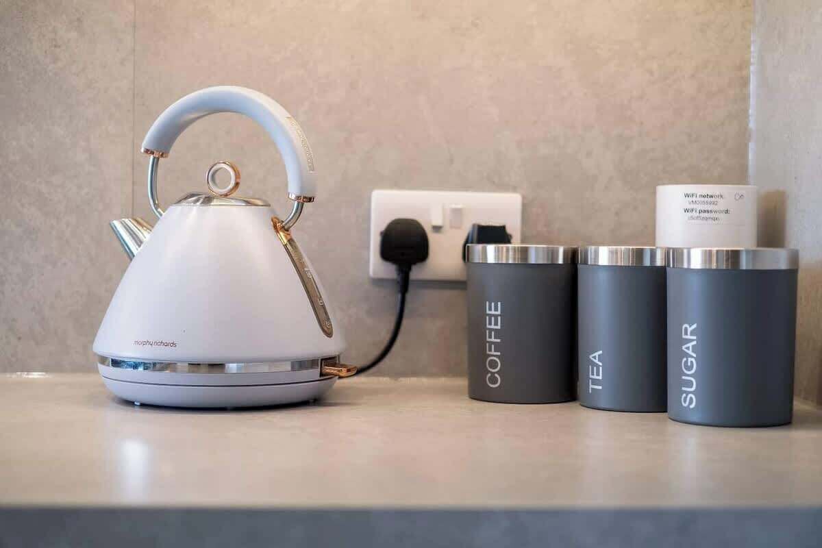 A white kettle, a power outlet, and two labeled containers on a countertop.