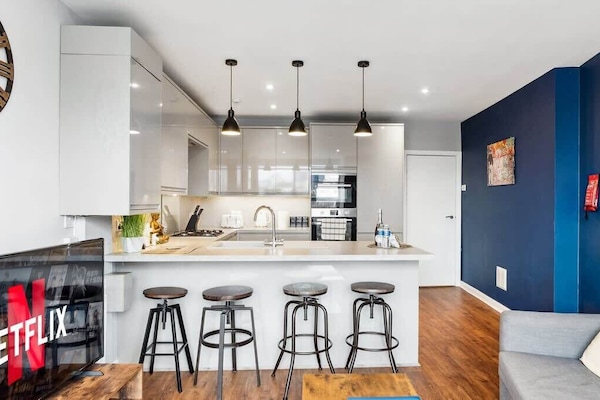 Bright, open-plan lounge and kitchen with a warm, relaxed feel. Comfortable seating, smart TV, and a kitchen island with bar stools create an easy space to unwind, cook, and socialise.