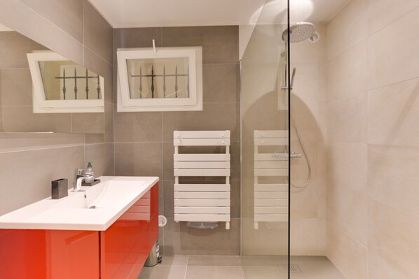 A modern bathroom with a white sink, red vanity, and a glass-enclosed shower area.