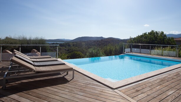 A wooden deck with a pool and lounge chairs overlooking a mountainous landscape. - Padulaccia by Pinarello Villa Services (Sainte-Lucie de Porto-Vecchio)