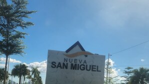 Un panneau indiquant l’entrée de Nueva San Miguel, avec un ciel dégagé et des palmiers en arrière-plan.