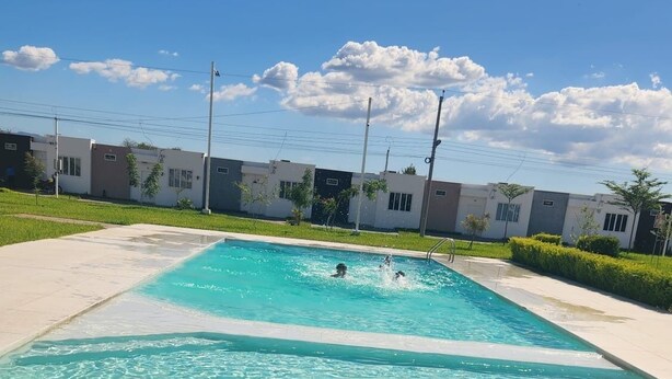 Une piscine à l’eau claire, entourée d’une terrasse carrelée et d’une pelouse.