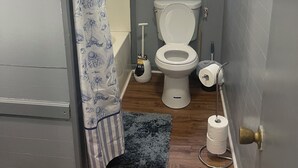 Un baño pequeño con inodoro, cortina de ducha, ventana con persianas y un dispensador de papel higiénico.