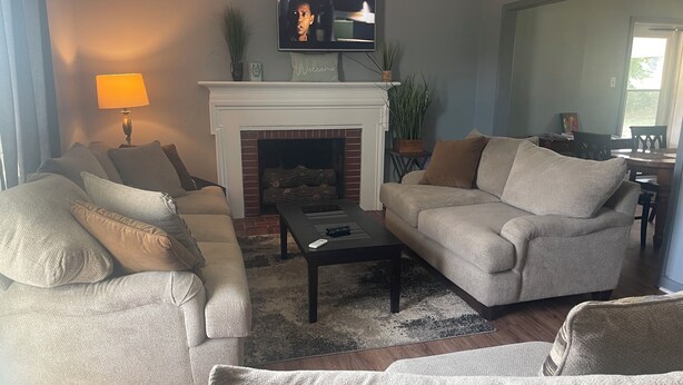 Una sala de estar con chimenea, dos sofás, una mesa de centro y un televisor sobre la chimenea.