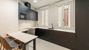 A modern kitchen with dark cabinets, a white countertop, and a window with a view. - Alameda estudio deluxe (Sevilla)