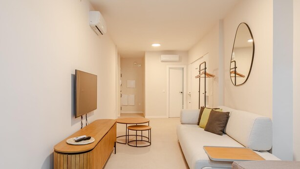 A modern living room with a sofa, a TV, a wooden cabinet, and a small table. - Alameda estudio deluxe (Sevilla)