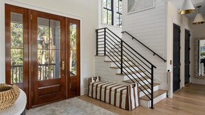 A spacious living area with a wooden staircase, a large rug, and a chandelier.