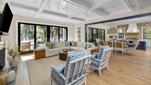A spacious living room with a large sofa, patterned chairs, and a dining area with a brick accent wall.