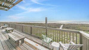 A wooden deck with benches and chairs overlooking a beach.