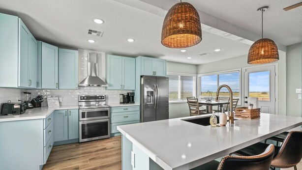 A modern kitchen with light blue cabinets, stainless steel appliances, and a large island with bar stools.