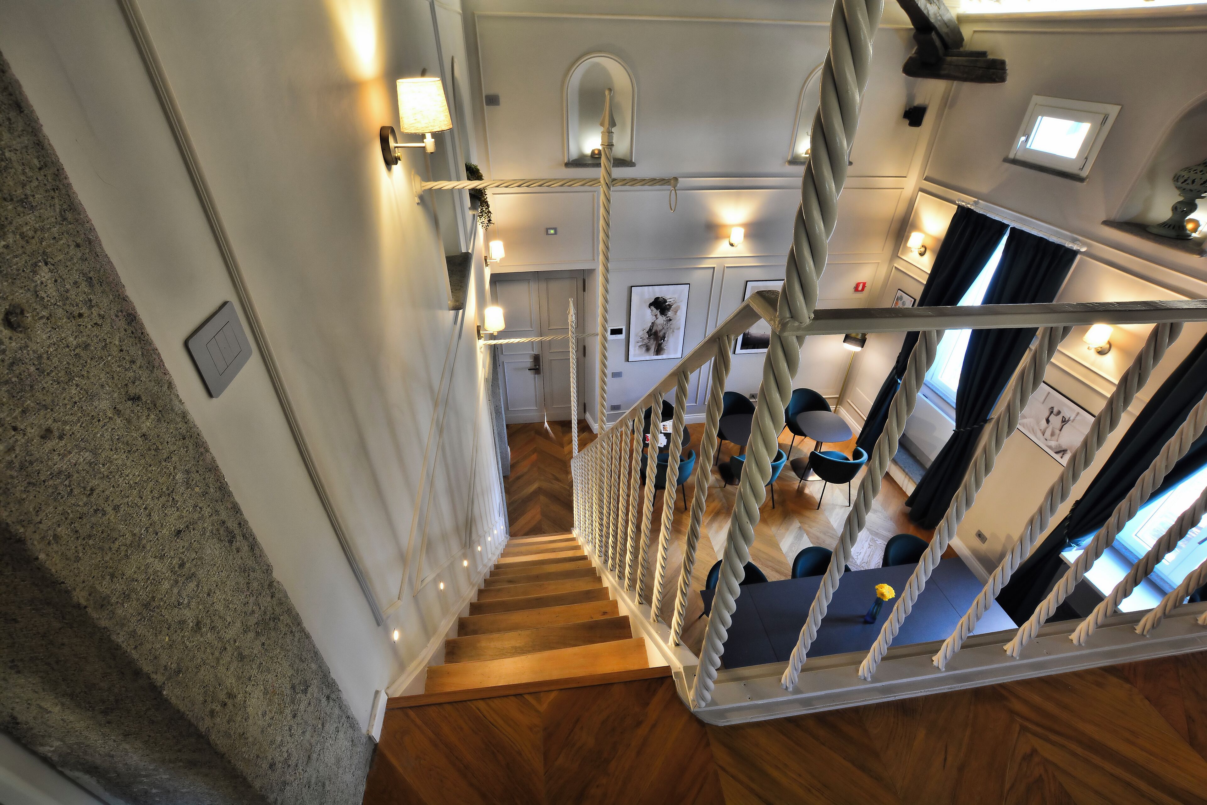 Un intérieur d’hôtel à plusieurs niveaux, avec un escalier en bois, un coin repas avec des chaises bleues et un espace cuisine.