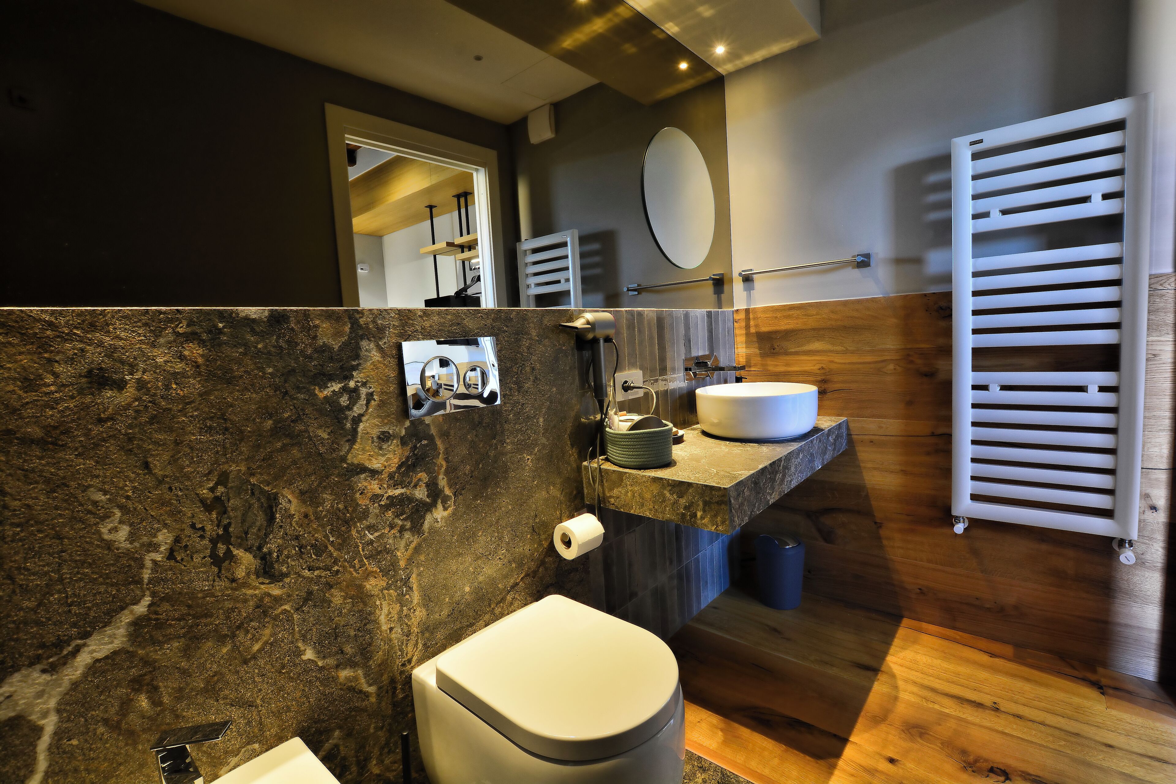 Une salle de bain moderne avec un mur en marbre, un meuble-lavabo en bois, un lavabo blanc et un porte-serviettes.