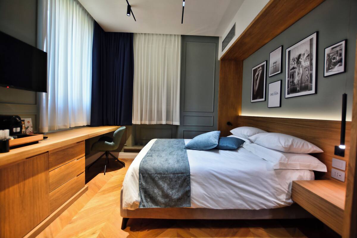 Una habitación de hotel moderna con un escritorio de madera, una cama con ropa de cama blanca y azul, y una pared con cuadros enmarcados.
